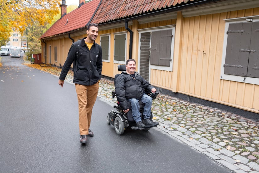 personlig assistent går bredvid rullstolsburen assistansanvändare